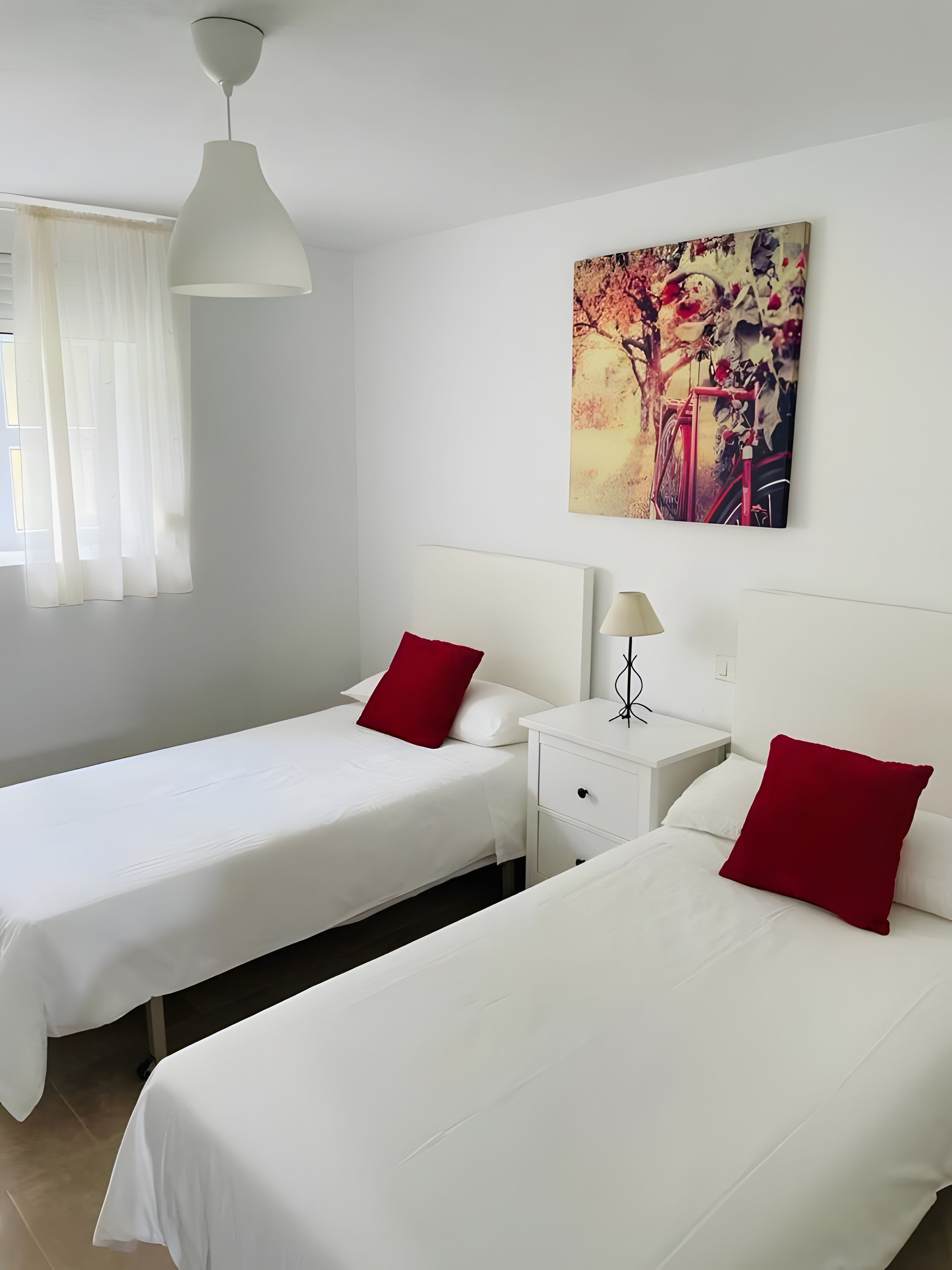 Una habitación de hotel con dos camas, una mesita de noche, una lámpara y un cuadro en la pared.