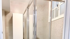Ein Badezimmer mit Duschkabine aus Glas, einer weißen Toilette und einer grünen Fußmatte.