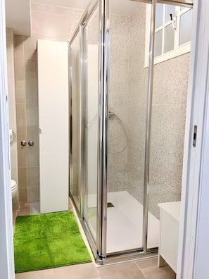 Un bany amb plat de dutxa de vidre, un vàter blanc i un estri de bany verd.