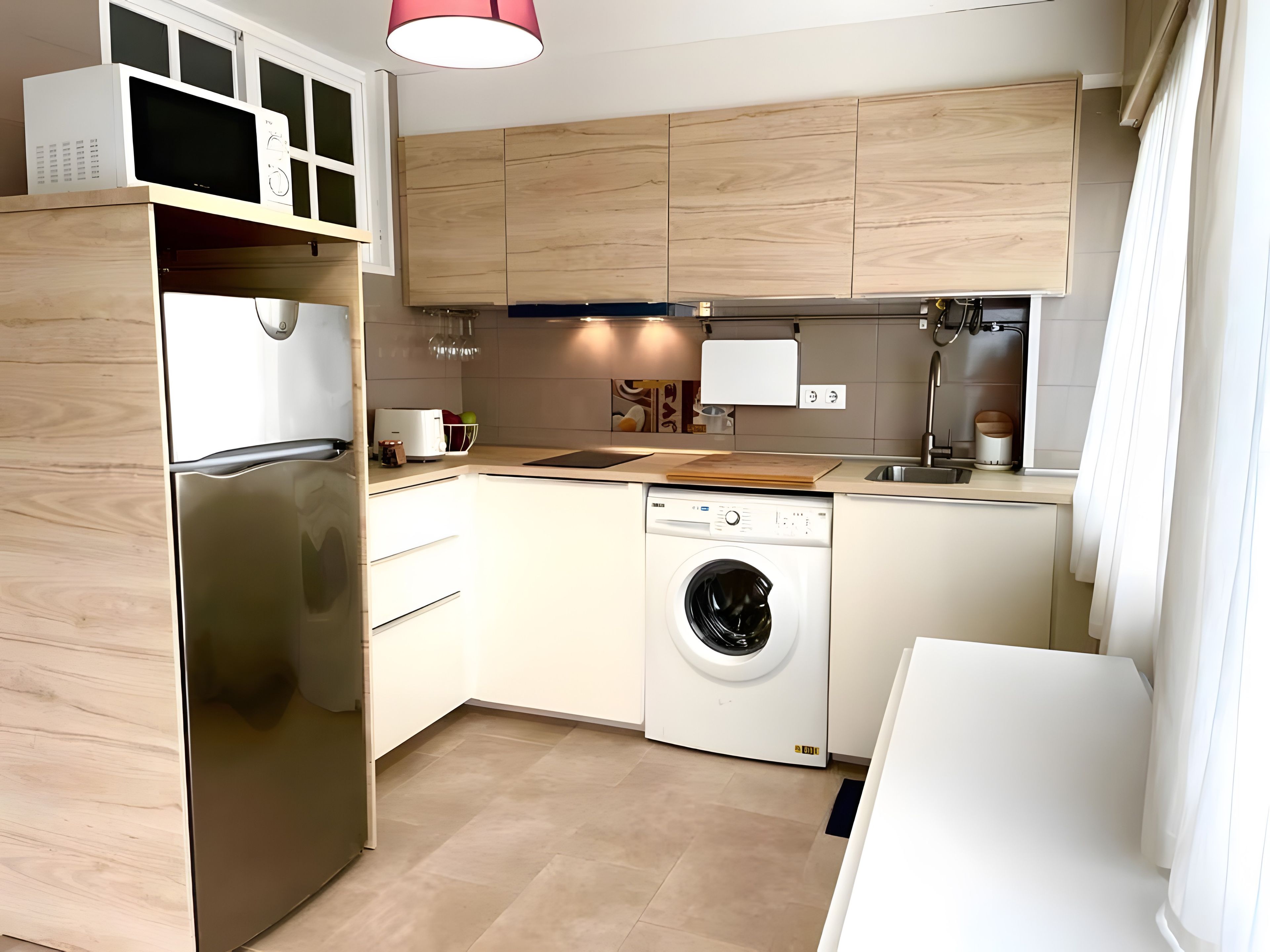 Una cocina moderna con un refrigerador de acero inoxidable, lavavajillas integrado, armarios de madera y un lavamanos.