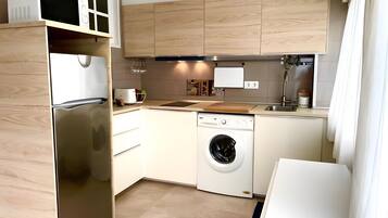 Una cocina moderna con un refrigerador de acero inoxidable, lavavajillas integrado, armarios de madera y un lavamanos.