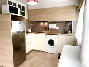 A modern kitchen with a stainless steel refrigerator, a built-in dishwasher, wooden cabinets, and a sink.