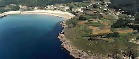 An aerial view of a coastal area with a beach, rolling hills, and scattered buildings.