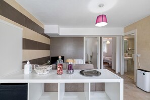 A modern kitchen with a white countertop, a pink pendant light, and a view into a bedroom.