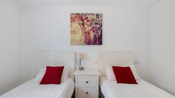 Un dormitorio con dos camas, cada una con una almohada roja, una mesita de noche con una lámpara y un cuadro en la pared.