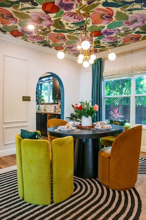 A dining area with a round table, chairs, a chandelier, and a floral ceiling. - Art Deco Designer Home + Jacuzzi, Walk to Beach (Hollywood)