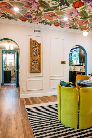 A room with a wooden floor, a striped rug, a green sofa, a white door, and a ceiling with floral wallpaper. - Art Deco Designer Home + Jacuzzi, Walk to Beach (Hollywood)