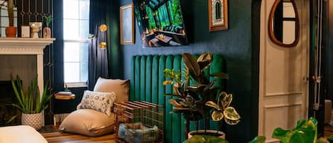 Uma sala de estar aconchegante com piso de madeira, um sofá, um radiador verde e diversas plantas.