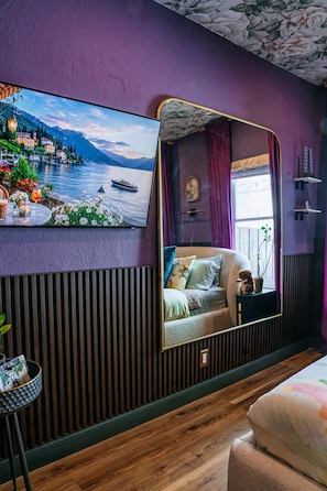 A bedroom with a large bed, a bedside table, a mirror, and a wall-mounted TV displaying a scenic view. - Art Deco Designer Home + Jacuzzi, Walk to Beach (Hollywood)