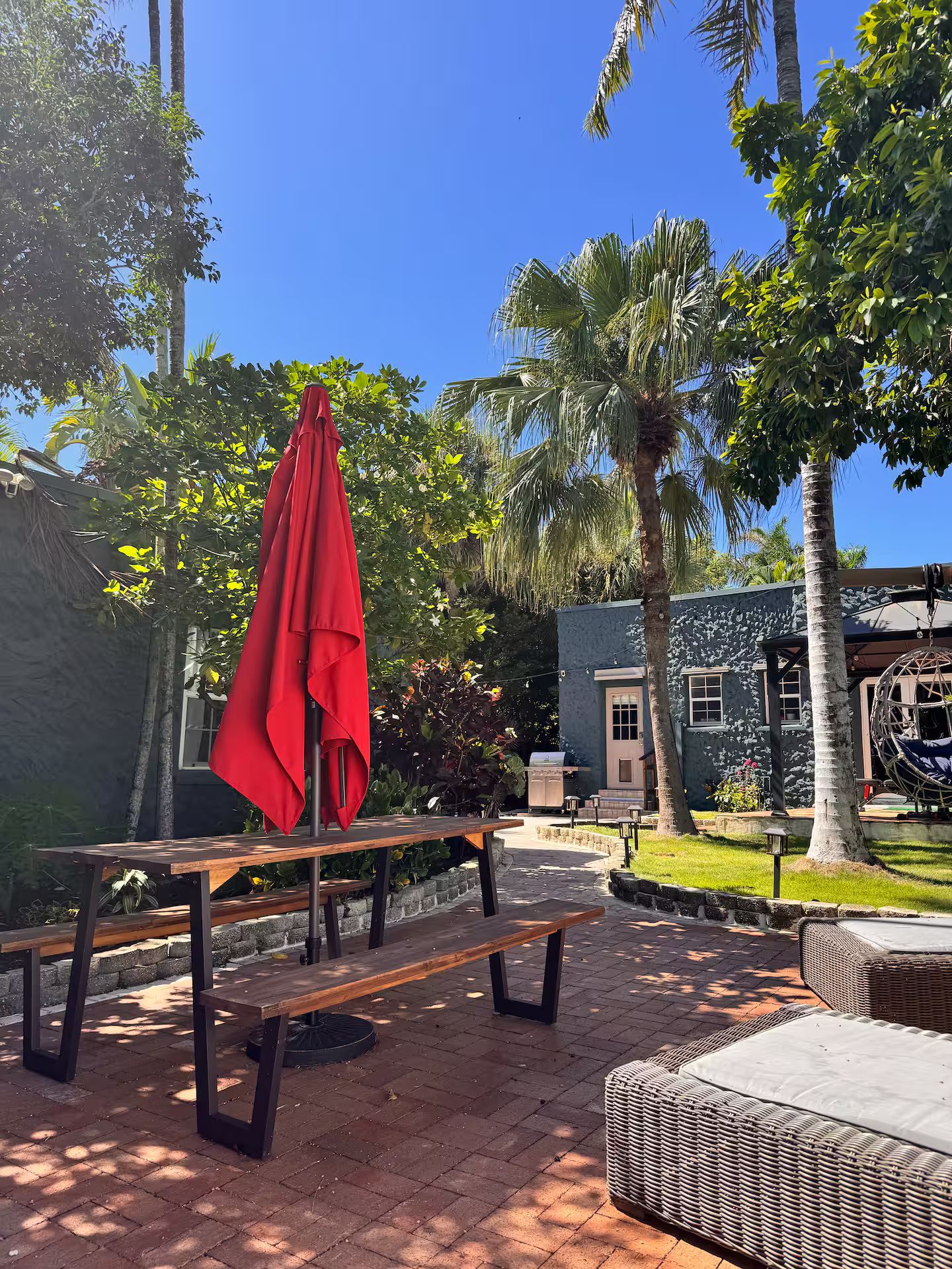 An outdoor patio area with picnic tables, a red umbrella, and a building with a stone facade.