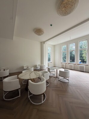 A spacious room with a high ceiling, large windows, and a variety of seating arrangements including round tables and chairs. - Parkhotel & Wellness Madeleine (Bavel)