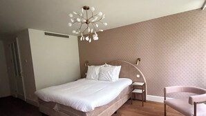 Une chambre à coucher comprenant un lit, une table de chevet, une chaise et un luminaire au plafond original.