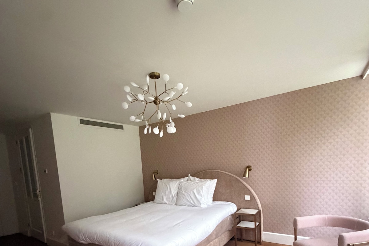 A bedroom with a bed, bedside table, chair, and a unique ceiling light fixture.