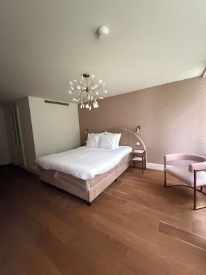 A bedroom with a bed, bedside table, chair, and a unique ceiling light fixture. - Parkhotel & Wellness Madeleine (Bavel)