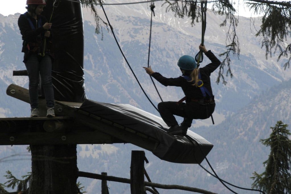 A zip-lining activity with participants on a platform and a mountainous backdrop.