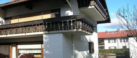 A two-story residential building with a balcony, a satellite dish, and a small garden area.