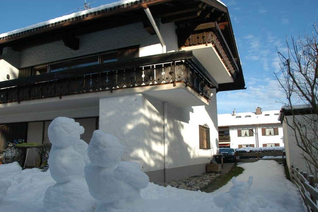 A two-story building with a balcony, snow accumulation around the base, and a clear sky.