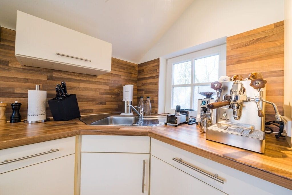 Una cocina moderna con armarios de madera, una cafetera espresso integrada y un ventanal que proporciona luz natural.