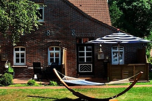A brick building with a number '8' on the facade, a door with a geometric design, and a hammock in the foreground. - Holiday apartment with 1 bedroom (Borkum)