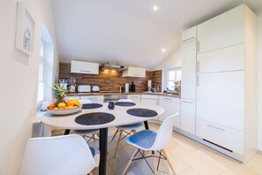 A modern kitchen with white cabinets, a dining table with placemats, and a fruit bowl. - Holiday apartment with 1 bedroom (Borkum)