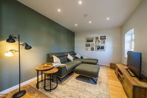 A modern living room with a sectional sofa, a coffee table, a floor lamp, a television, and a wall with framed pictures. - Holiday apartment with 1 bedroom (Borkum)