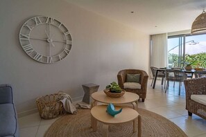 A modern living room with a large wall clock, wicker furniture, and a view to the outside.
