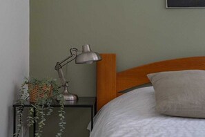A neatly made bed with a wooden headboard, a bedside table with a lamp, and a small plant.