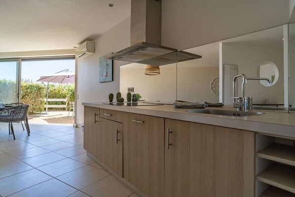 A modern kitchen with a large island, a built-in oven, and a window overlooking a patio area.