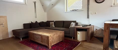 Un salón estilo loft con techo inclinado, vigas de madera, un conjunto de sofás, una mesa de centro y una alfombra.