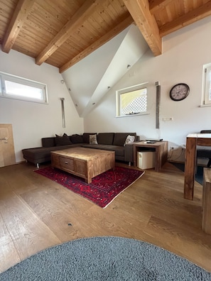 Un salón estilo loft con techo inclinado, vigas de madera, un conjunto de sofás, una mesa de centro y una alfombra.