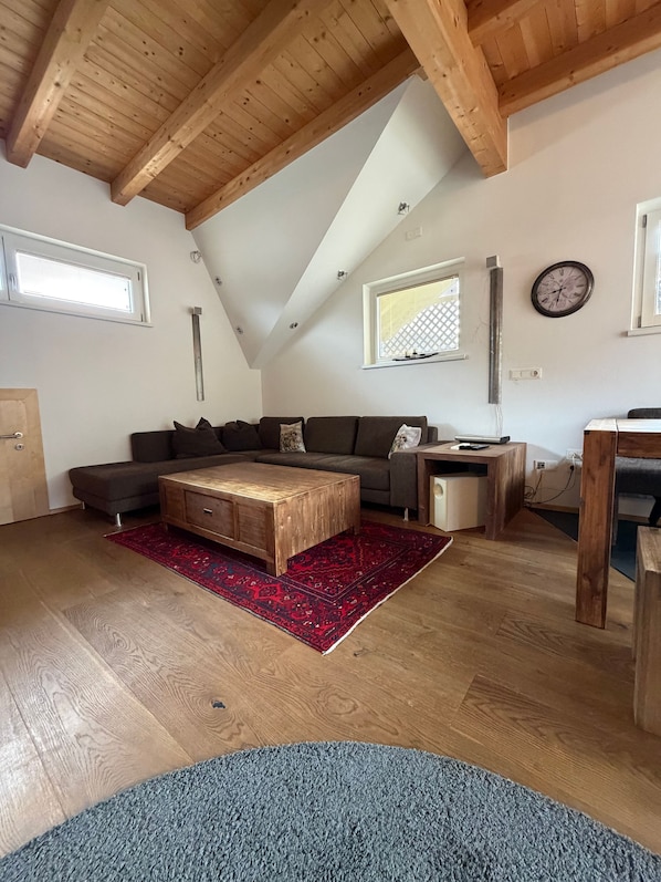 Een woonkamer in loftstijl met een schuine plafond, houten balken, een zithoek, een salontafel en een vloerkleed.