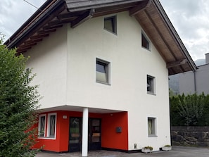 Een gebouw met twee verdiepingen, een gevel in rood en wit, meerdere ramen en een stenen muur op de achtergrond.