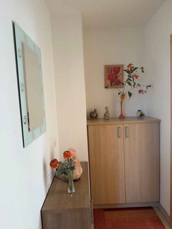 A room with a wooden cabinet, a mirror, a vase with flowers, and a painting on the wall.