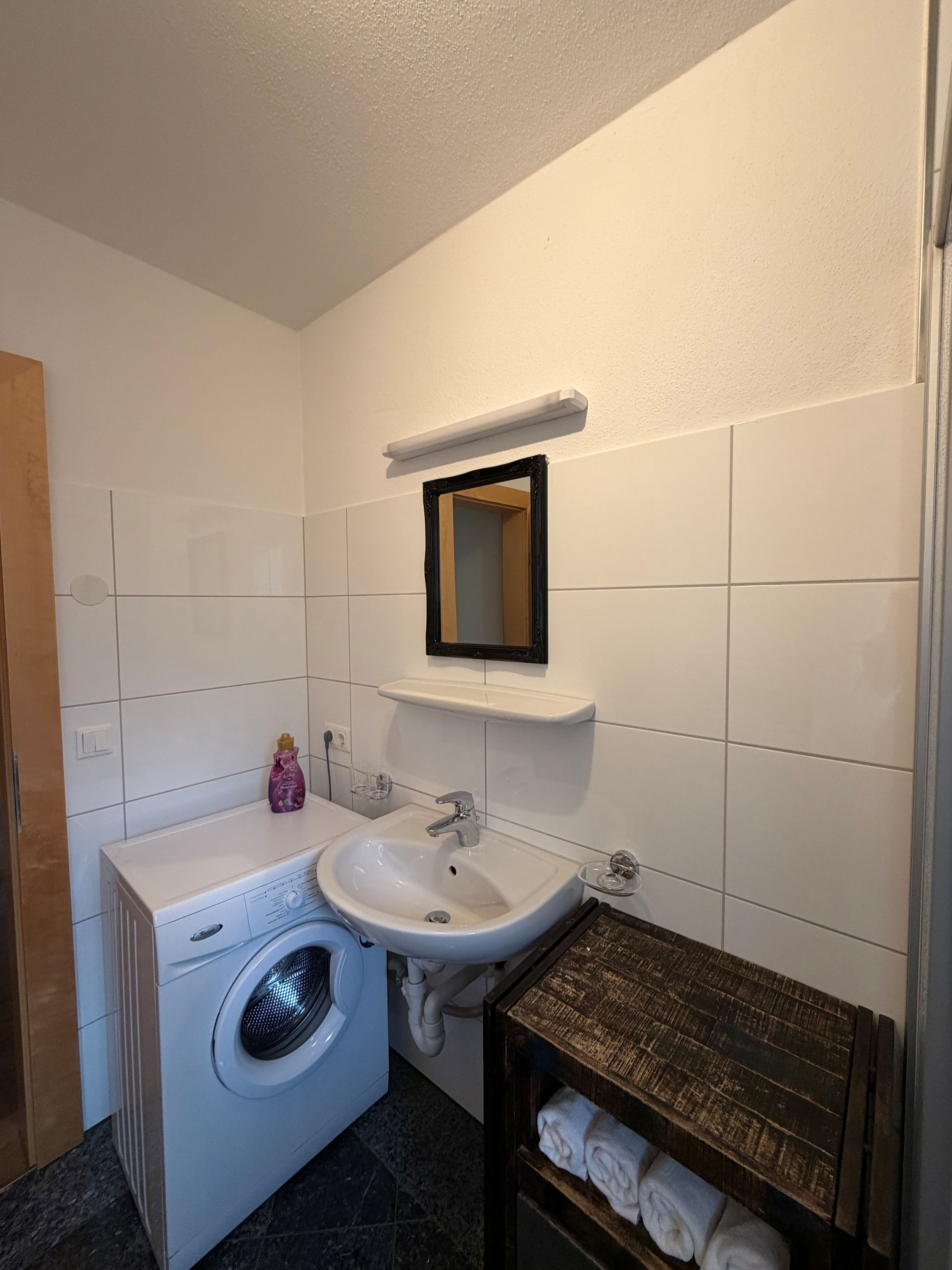 A compact bathroom with a washing machine, a sink, and a mirror.