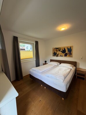 A bedroom with a bed, a window with curtains, a nightstand with a lamp, and a wall art piece.