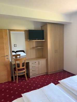 A compact hotel room with a bed, a desk with a chair, a wardrobe, and a television on a shelf.