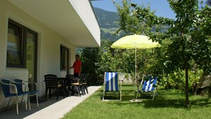 An outdoor seating area with a table and chairs, a yellow umbrella, and a view of a mountain. - Apartment Markus: Gartenwohnung mit Bergblick, privatem Garten, WLAN & Spa (gegen Aufpreis) (Ried im Zillertal)