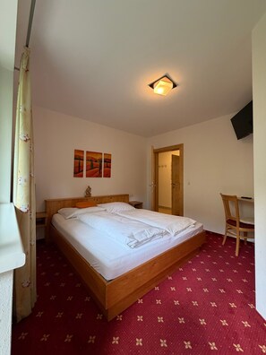 Un dormitorio con cama, escritorio, silla y televisión en la pared.