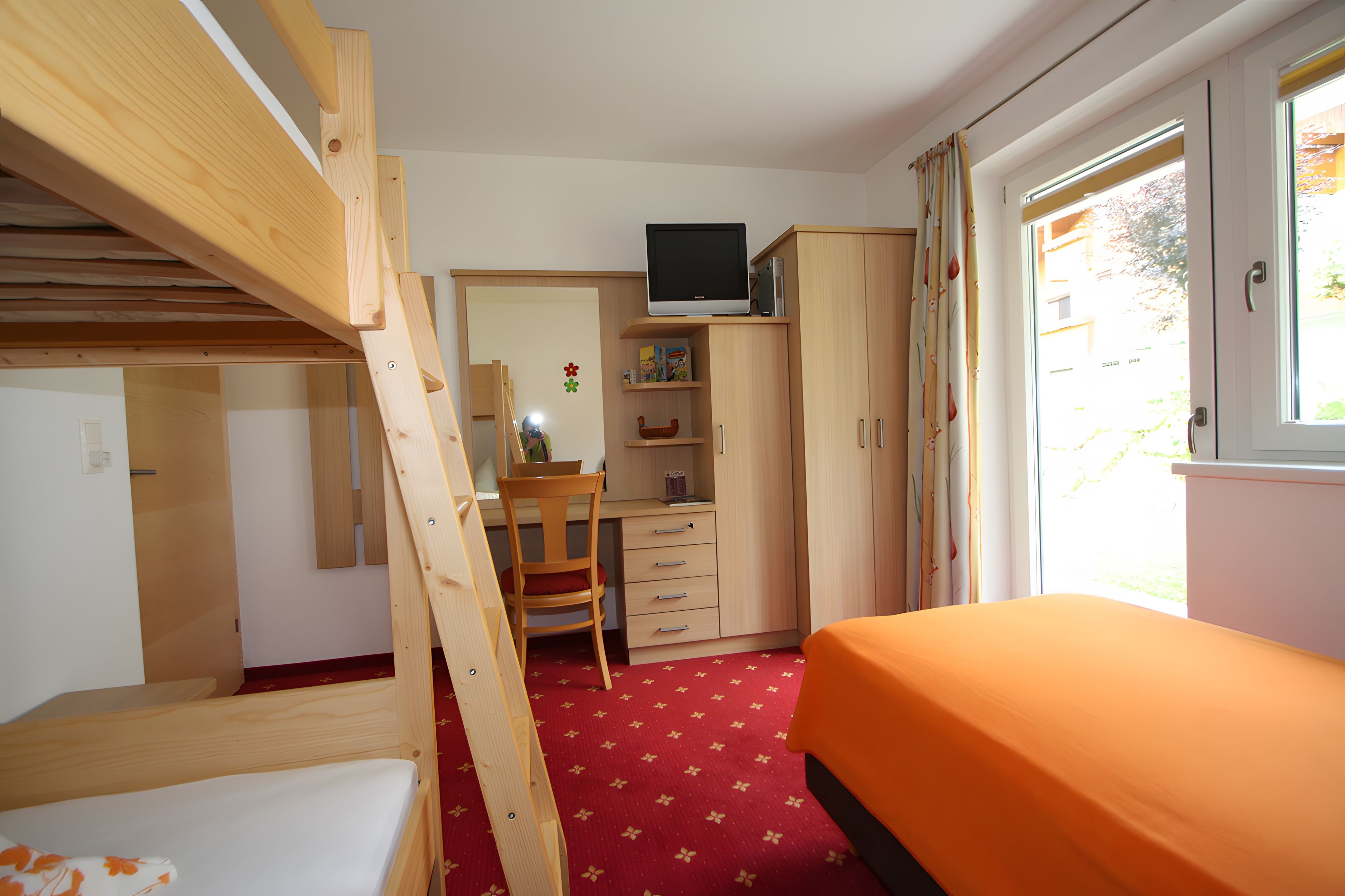 Ein Zimmer mit einem Etagenbett, einem Schreibtisch mit Stuhl, einem Kleiderschrank und einem Fernseher darauf.