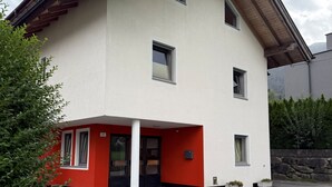 A two-story building with a red and white facade, multiple windows, and a stone wall in the background. - Apartment Markus: Gartenwohnung mit Bergblick, privatem Garten, WLAN & Spa (gegen Aufpreis) (Ried im Zillertal)