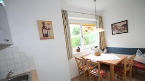 A kitchen with a dining table, chairs, a window with curtains, and a sink. - Apartment Markus: Gartenwohnung mit Bergblick, privatem Garten, WLAN & Spa (gegen Aufpreis) (Ried im Zillertal)