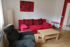 A living room with a red sofa, a grey sofa, a wooden coffee table, and a red rose painting on the wall. - Holiday apartment with 1 bedroom (Klotten)