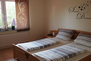 A bedroom with two single beds, a bedside table with a lamp, a window with blinds, and a wall decoration with stars and the words 'Sweet Dreams'. - Holiday apartment with 1 bedroom (Klotten)