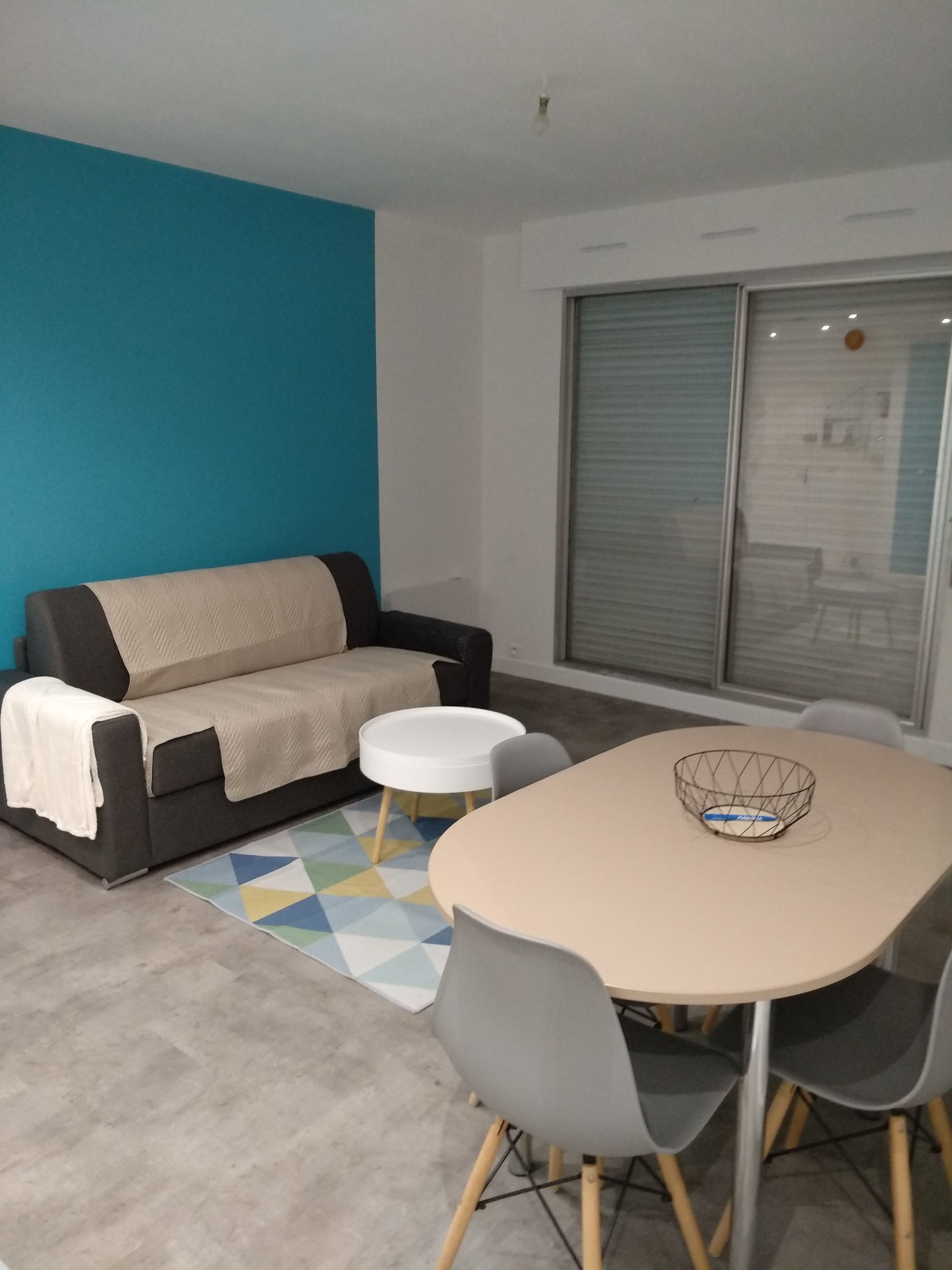 A modern living room with a sofa, a small round table, and a dining table with chairs.