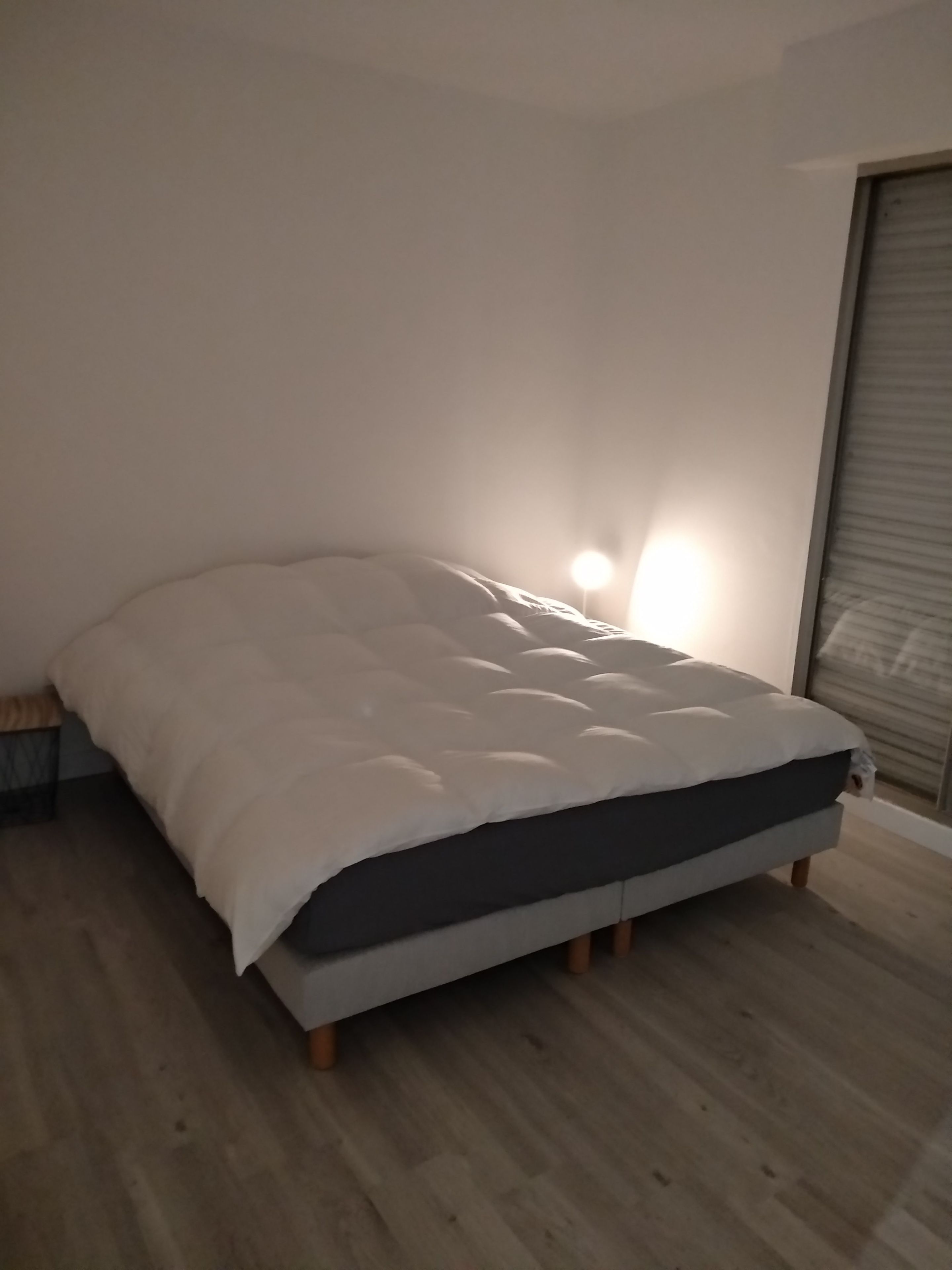Une chambre à coucher avec un lit, un plancher en bois et une fenêtre avec des stores.