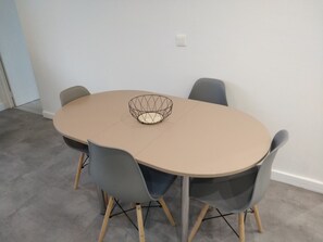 Una mesa redonda con un centro de mesa tejido, rodeada por cuatro sillas con patas de madera y tapicería gris.