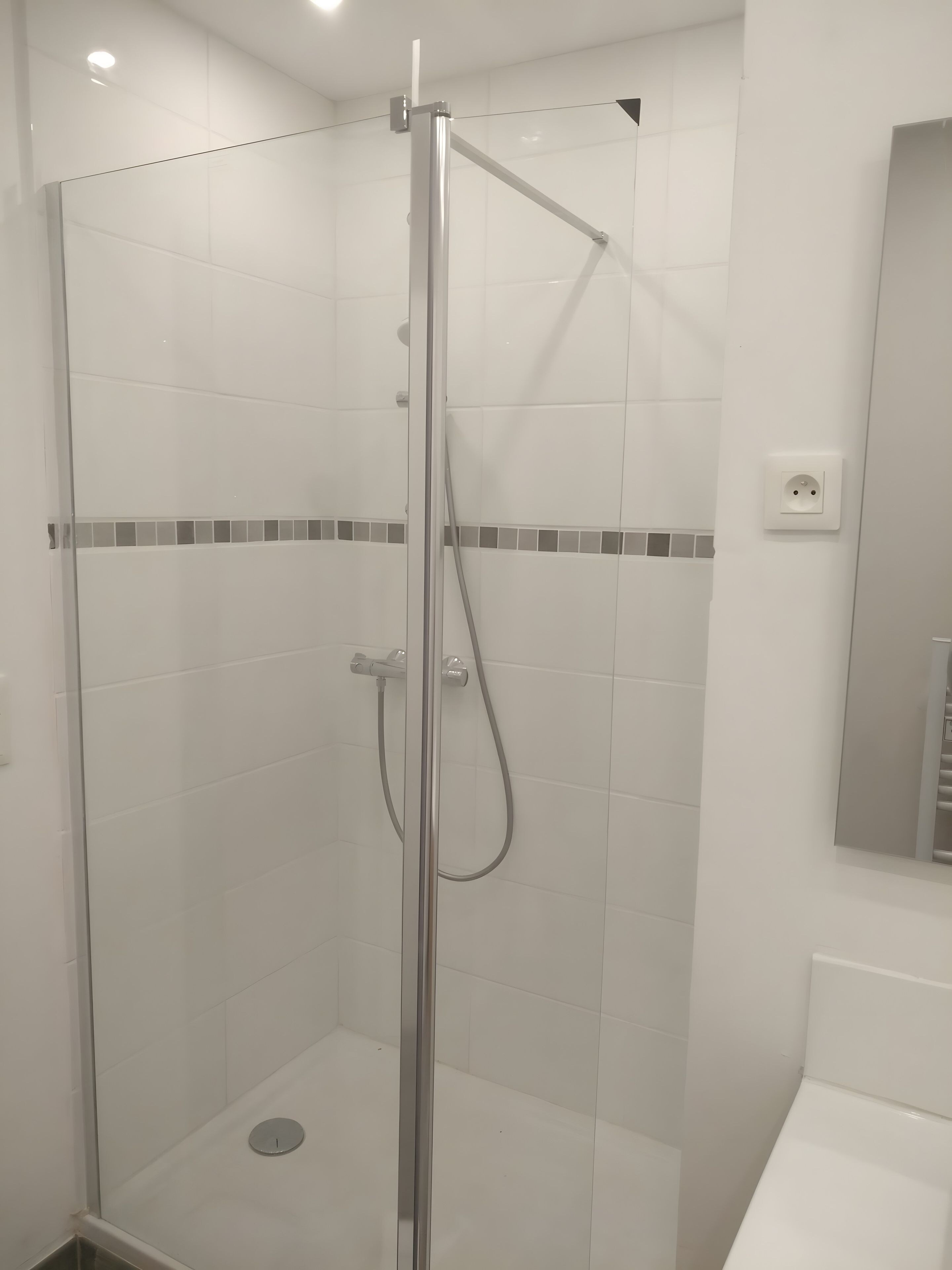 A glass-enclosed shower stall with a handheld showerhead and a wall-mounted faucet.