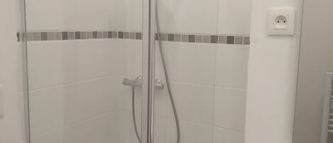 A glass-enclosed shower stall with a handheld showerhead and a wall-mounted faucet.