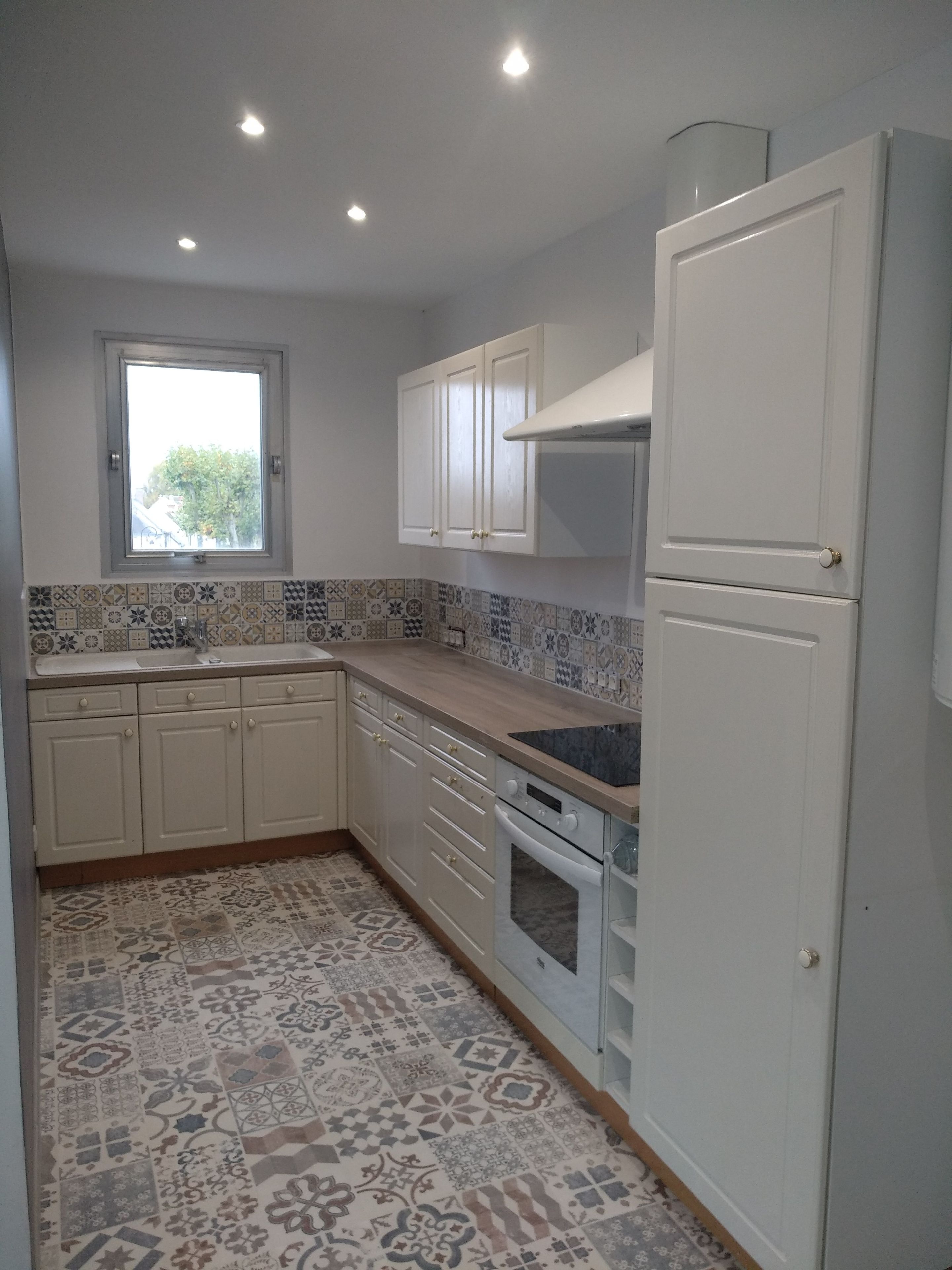 A kitchen with white cabinets, a window, and patterned floor tiles.