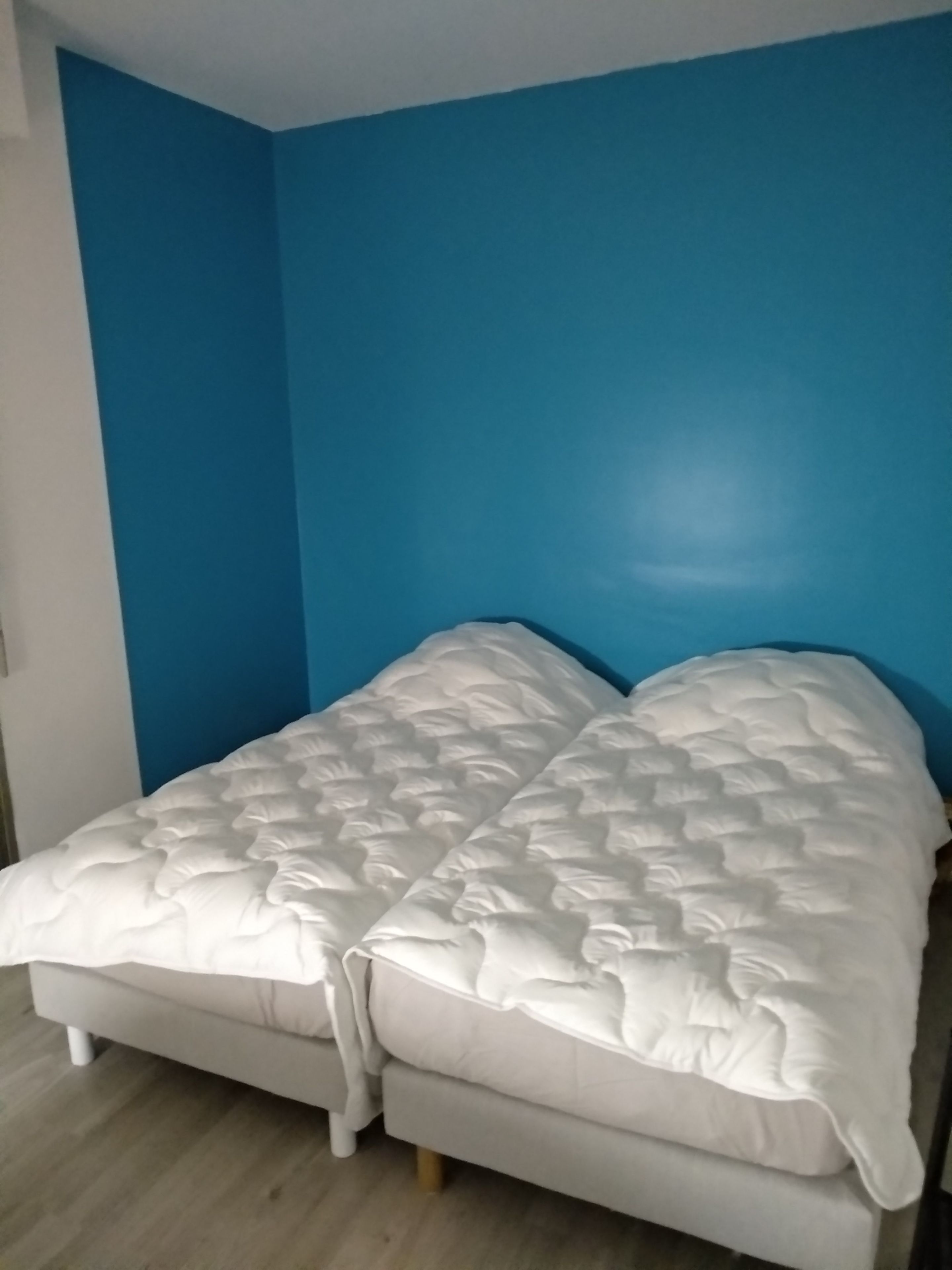 A room with a bed against a blue wall, wooden flooring, and a white headboard.